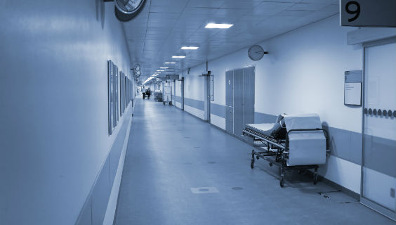 Blåtonet billede af en seng på en hospitalsgang